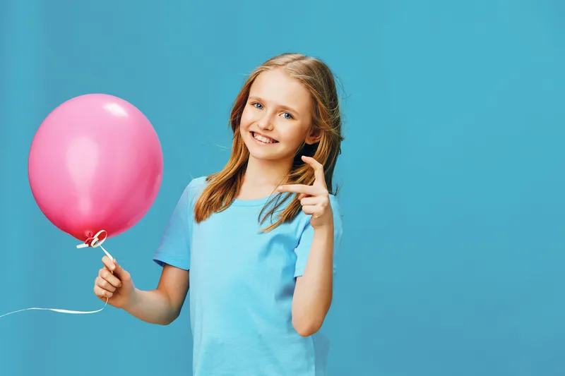 Happy girl holding a pink balloon against a bright blue background, showcasing joy and innocence, perfect for children s celebrations and fun events