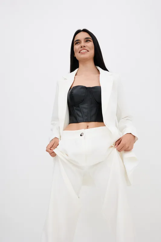 young woman in white suit and black corset smiling confidently, standing on plain white background, fashionable and modern style outfit, studio lighting