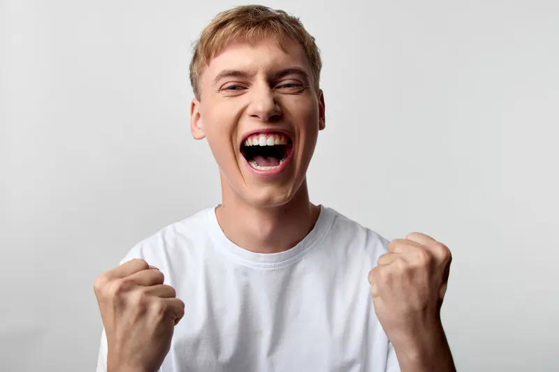 Excitement, celebration, energy, enthusiasm, victory, cheering, male in white tee with clenched fists, shouting with joy, dynamic moment for achievement, motivation, and success in a studio stock