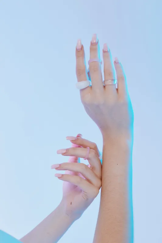 Close-up of a woman’s hands with long manicured nails and stylish rings against a soft blue background. Concept of beauty, fashion, elegance, and self-care.
