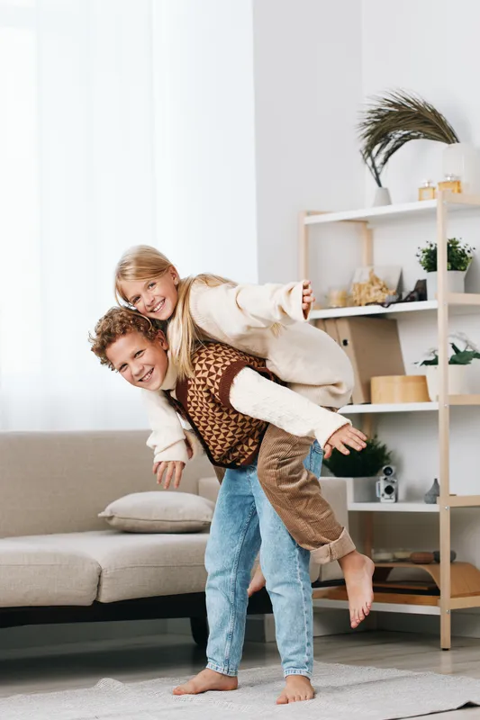 Joyful couple enjoys a playful moment indoors with a piggyback ride, laughter, and warmth. Light fills a modern living room, creating a candid, affectionate scene that captures connection, energy,