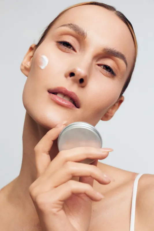 Close-up of a woman applying cream to her cheek, soft lighting, natural tones, fresh glow, skincare moment, calm expression, hydration focus, simple routine