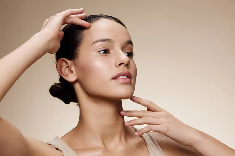 A young woman with smooth skin, showcasing skincare routine, natural beauty, and self care, wearing a neutral sleeveless top against a soft beige background
