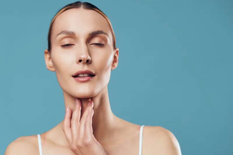 Woman skincare beauty portrait face studio touching calm expression, young woman holding cheeks, smooth skin, soft studio light, minimal blue background, close up beauty care, routine