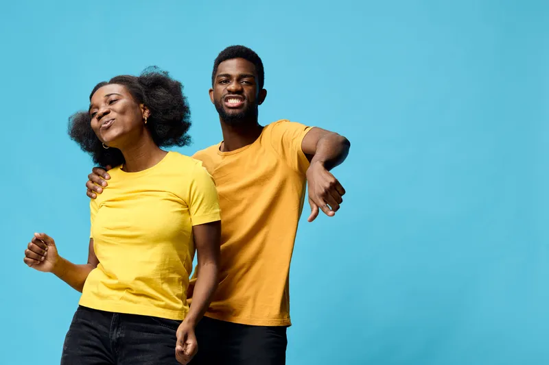 A joyful African couple wearing yellow t shirts, dancing against a bright blue background, radiating happiness and connection in a vibrant, seasonal celebration