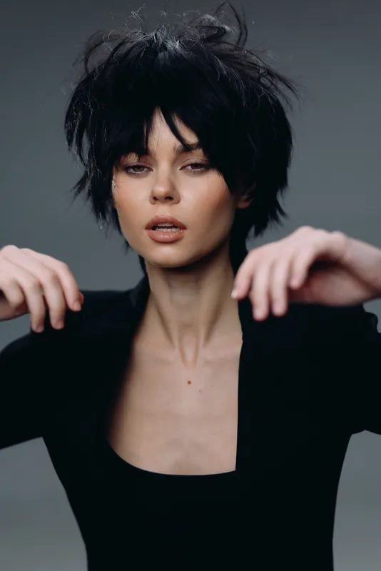 Young woman with short black hair wearing black outfit looking confidently with a gray background