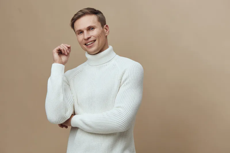 smiling man wearing white turtleneck sweater look camera with joy happy caucasian young male casual clothing isolated on beige background digital detox concept