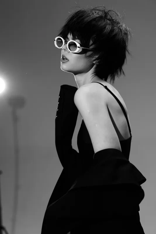Stylish woman in black dress and white sunglasses posing in black and white fashion portrait