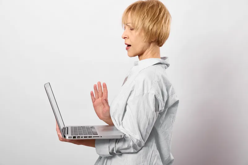 Woman short blond hair with laptop, technology stop hand gesture, security privacy concept in office, serious focused expression, refusal message, warning signal