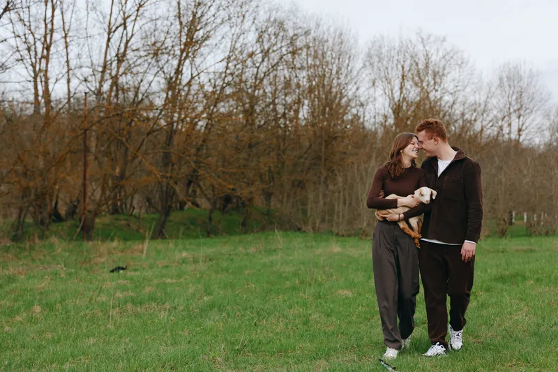 A couple strolls through a grassy park, sharing a warm moment with their dog nearby, casual clothes and a relaxed vibe. A lifestyle shot capturing affection, companionship, and everyday love in a