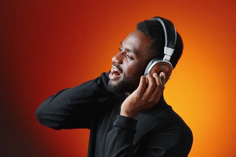 A joyful young Black man enjoying music while wearing headphones against a vibrant orange background, showcasing emotions of happiness and relaxation