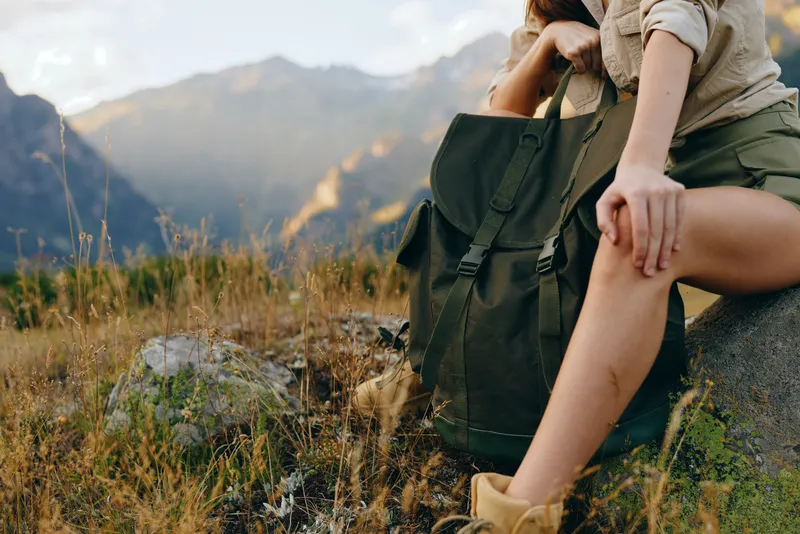 Woman lifestyle traveler sitting on rock with backpack resting in nature, mountain landscape background, casual outfit, outdoor adventure, peaceful moment.