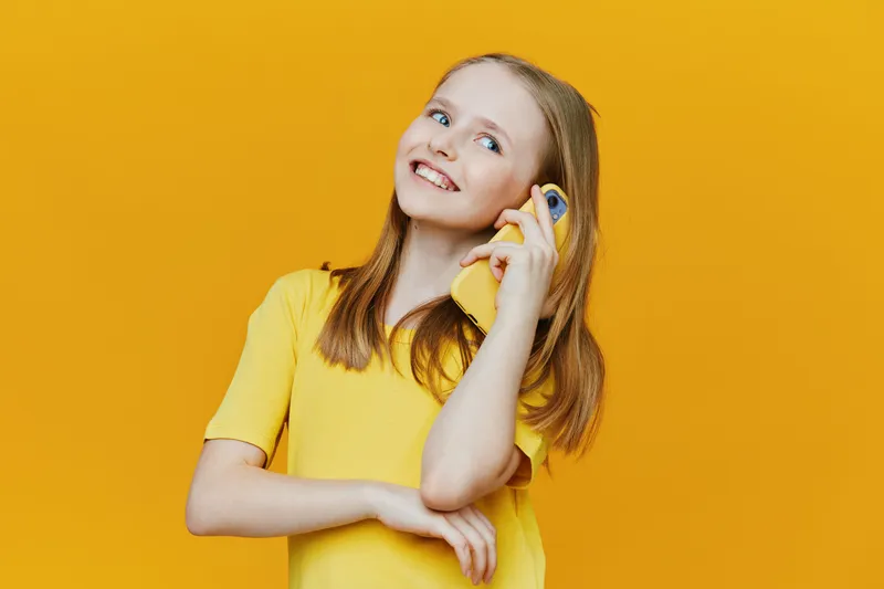 Happy girl talking on a yellow phone against a vibrant yellow background, showcasing joy, connection, and youthful communication with modern technology