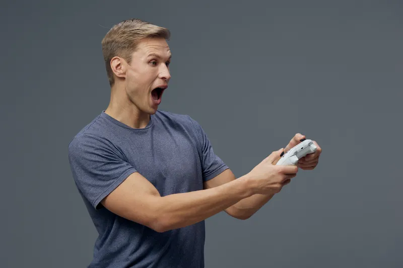 Excited young caucasian man holding game controller surprised open mouth gray background esports digital entertainment concept