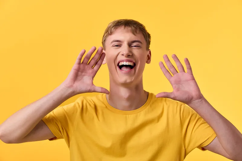 Joyful man in a bright yellow shirt against a vivid yellow background, arms raised and smiling wide, conveying energy, happiness, and friendly enthusiasm.
