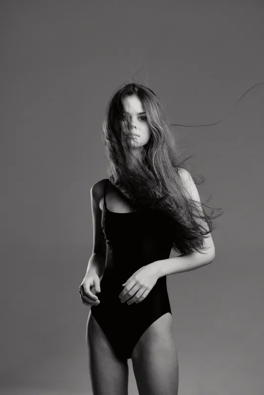 Black and white portrait of a young woman in a black bodysuit with flowing hair and serious expression