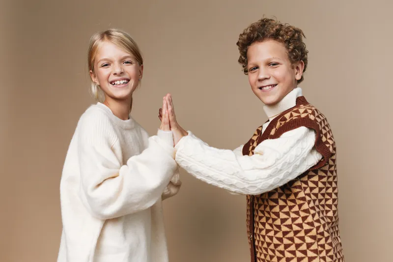 Authenticity drives a warm, candid moment as two youths share a high five, framed in a cozy, school inspired lifestyle scene with soft textures and friendly smiles.