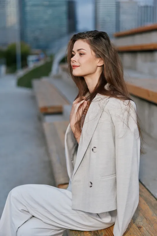 Business woman in a stylish suit, smiling confidently outdoors against a modern urban background, showcasing professionalism and elegance.