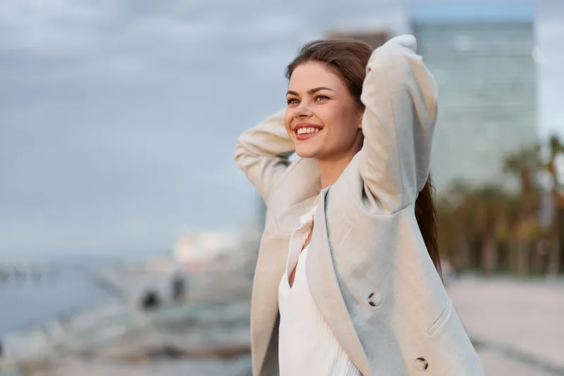 Confident businesswoman enjoying a sunny day outdoors with a contemporary cityscape in the background, radiating positivity and style.