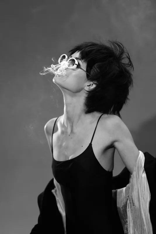 Black and white portrait of a stylish woman exhaling smoke with carefree attitude and fashion elegance