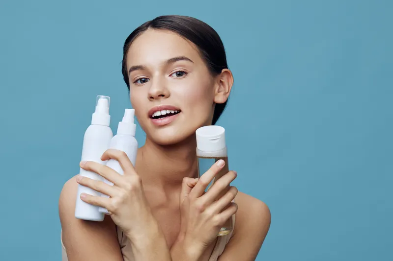 Young model showcasing hair care products with a bright smile, promoting healthy hair and beauty in a vibrant blue background