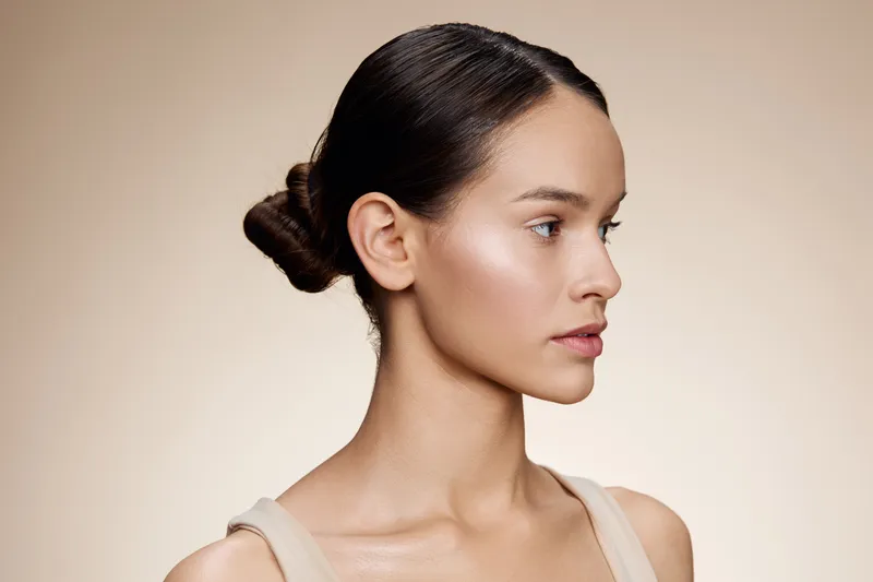 A profile shot of a young model with a neutral expression, showcasing flawless skin, natural makeup, and a clean background, perfect for beauty and skincare concepts