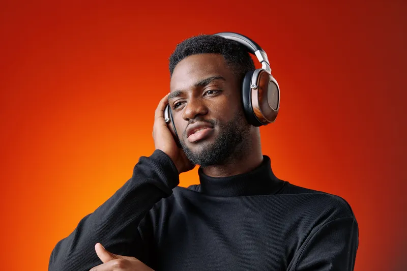 Young Black man enjoying music with headphones against a vibrant orange background, expressing relaxation and engagement in a modern style