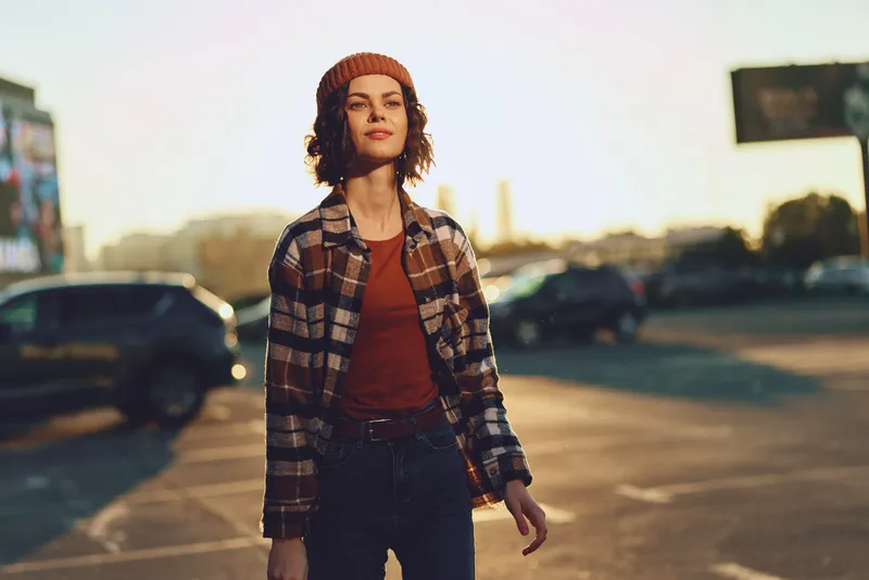 woman walking through an urban parking lot at golden hour, candid portrait of a confident young adult with authenticity and mindful living vibe, emotional storytelling in warm glow.