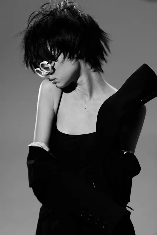 Black and white portrait of a stylish woman with short hair wearing sunglasses and a black dress, expressing elegance and mystery.