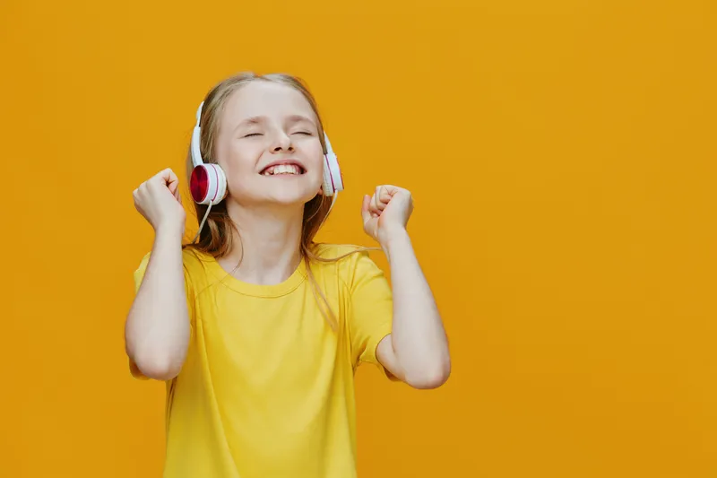 Happy girl listening to music with headphones on a bright yellow background, celebrating joy and positivity, perfect for illustrating childhood happiness and music themes