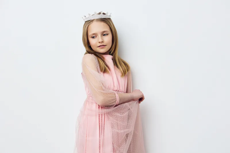 Cute young girl in a pink tulle dress with a tiara, displaying a gentle expression against a white background, perfect for children s fashion and portrait photography