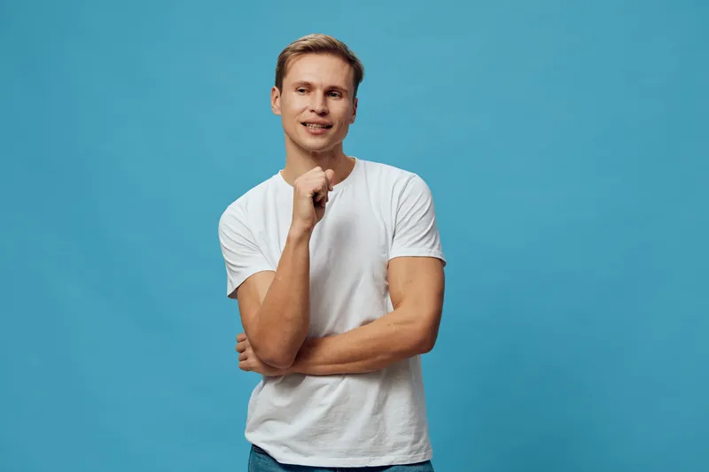 Smiling young man with blond hair, casual white t-shirt, standing confidently against a vibrant blue background. Joyful, relaxed, positive vibe, lifestyle concept, studio portrait, happy expression, i