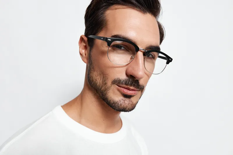 Confident young man wearing glasses and a white t-shirt looks directly at the camera with a stylish expression, isolated on a solid light background.