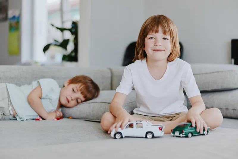 Happy boy playing with toy cars on a cozy couch, surrounded by soft furniture and a relaxed atmosphere, embodying childhood innocence and joy.