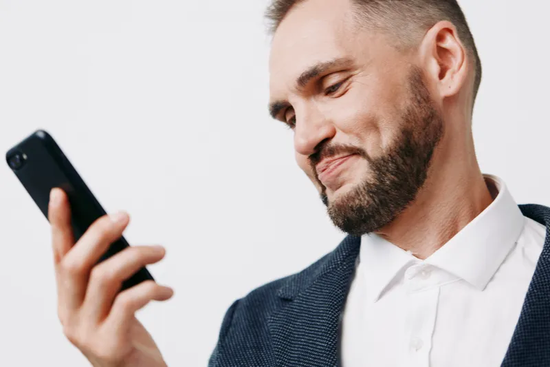 Portrait of a professional business man, smiling softly while looking at his phone, set against an isolated colorful background, conveying calm optimism and focused emotion.