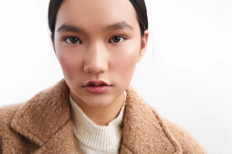 asian woman wearing a cozy coat faces the camera in a bright studio, exuding calm confidence and a ready-to-work attitude that suits a modern business setting, in this clean headshot style that