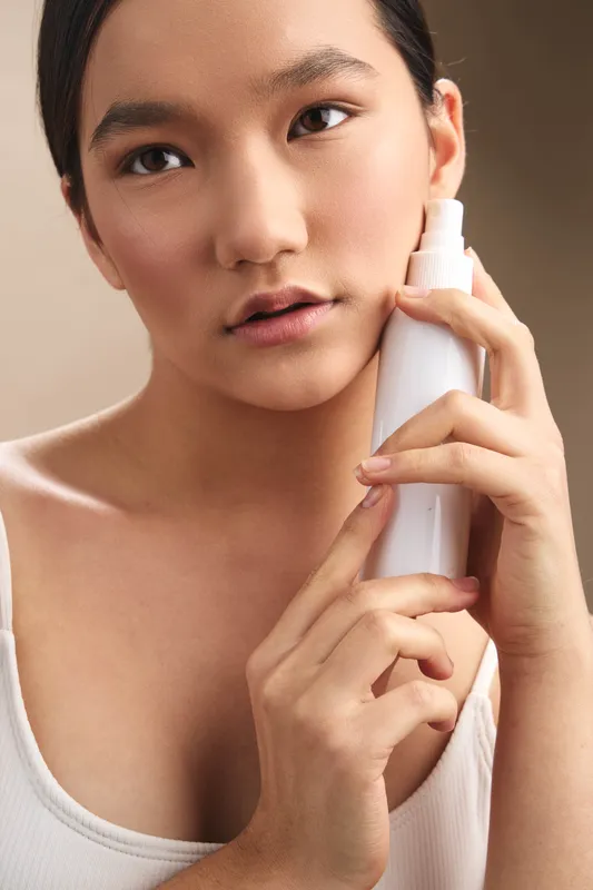 asian woman applies skincare product in a calm home setting, close up portrait with gentle light, thoughtful expression, creating a clean, confident wellness moment focused on self care and routine.