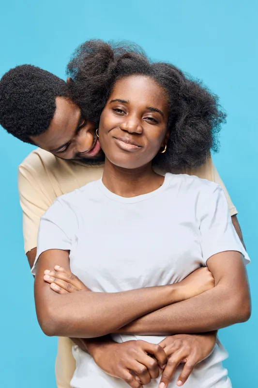 Happy couple embracing with a blue background, showcasing love and connection, featuring African descent models in casual attire, capturing a joyful moment