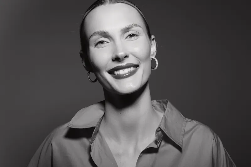 Smiling white woman with fair skin and earrings looks at camera in studio. Portrait with soft lighting and casual shirt. Concept for happiness and beauty.