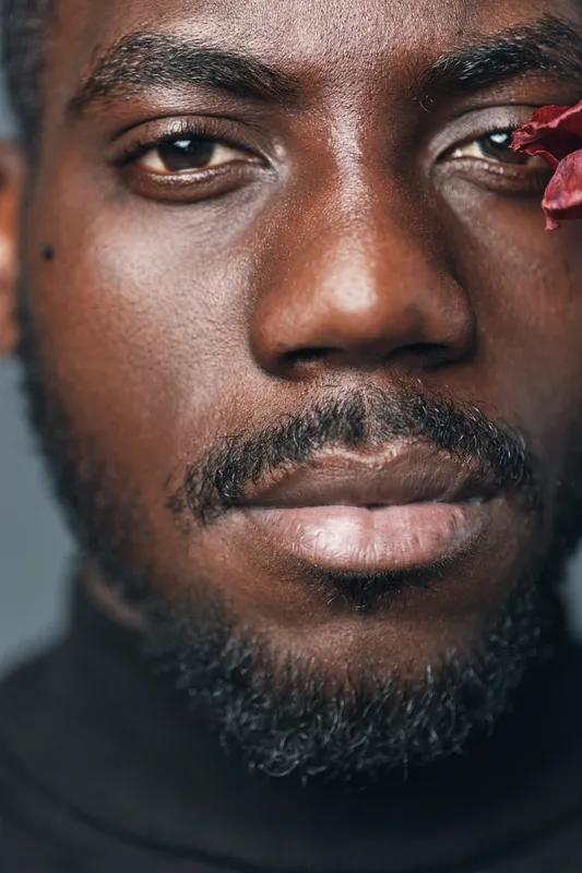 African man portrait closeup with beard and mustache wearing black turtleneck in creative conceptual visual style with flower petal on face for artistic expression and diversity.