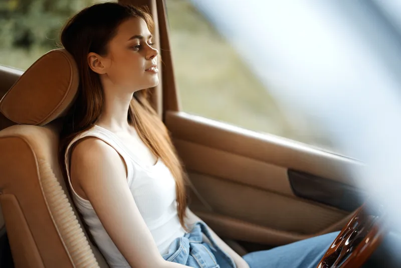 Young woman relaxing in a car, enjoying the tranquility of nature, with soft sunlight enhancing her peaceful expression and natural beauty.