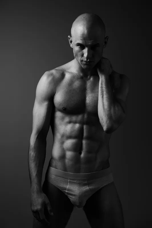 Black and white portrait of a muscular man conveying strength and confidence, showcasing his sculpted physique in dramatic lighting.