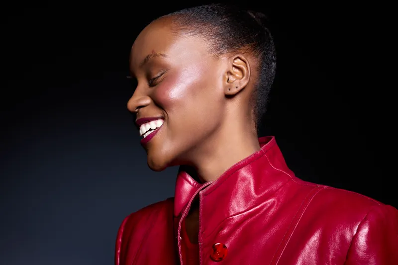 Profile of a smiling black woman with dark skin wearing a red leather jacket. She looks joyful and confident against a dark background. Concept of happiness and fashion.