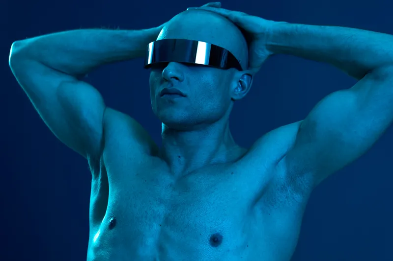 Stylish man with futuristic glasses posing dramatically, showcasing a striking blue light aesthetic. Captivating and eye-catching portrayal in modern fashion.