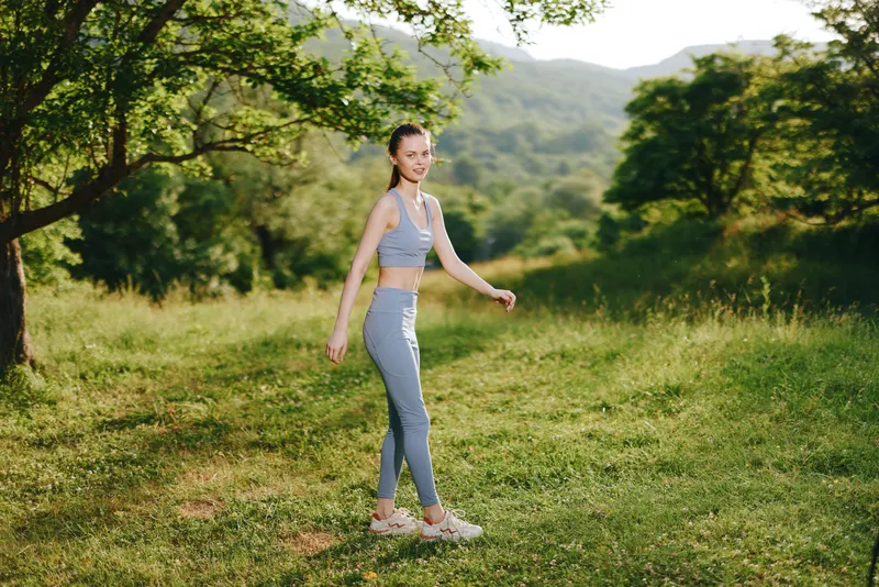 Young woman in sportswear walking through a green landscape, showcasing fitness and vitality, ideal for healthy lifestyle or outdoor activities themes
