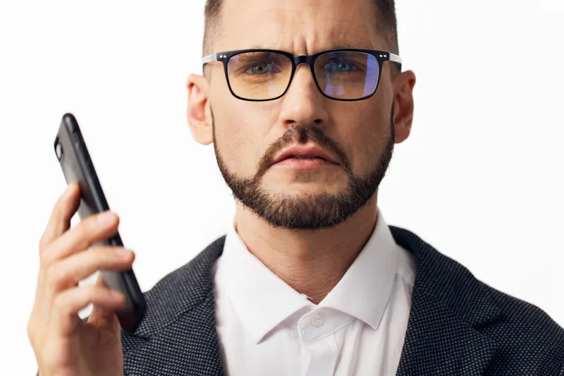 A professional business man with glasses stands in front of an isolated colored background, projecting thoughtful concern and controlled emotion, ideal for corporate communication and leadership