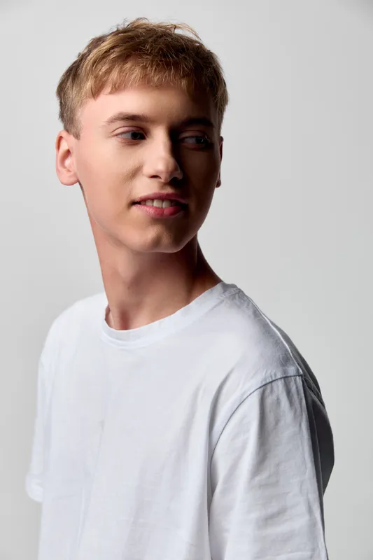 Young man in a white t shirt posed in a studio with soft lighting and a neutral background, showcasing casual fashion, relaxed mood, clean composition and everyday style.