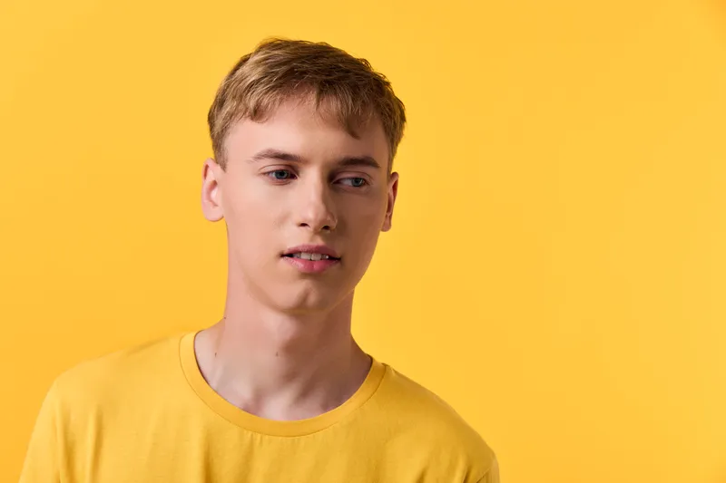 Male with short blond hair wearing a yellow t shirt against a bright yellow backdrop, relaxed expression, studio shot, minimalist style, clean lighting, bold color mood for lifestyle and marketing