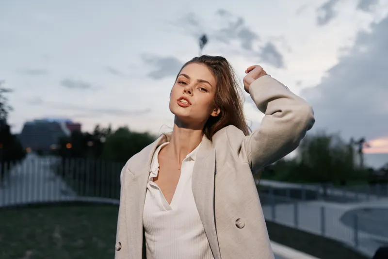 Confident businesswoman outdoors wearing a light coat, showcasing empowerment and urban style with a dramatic sky backdrop.