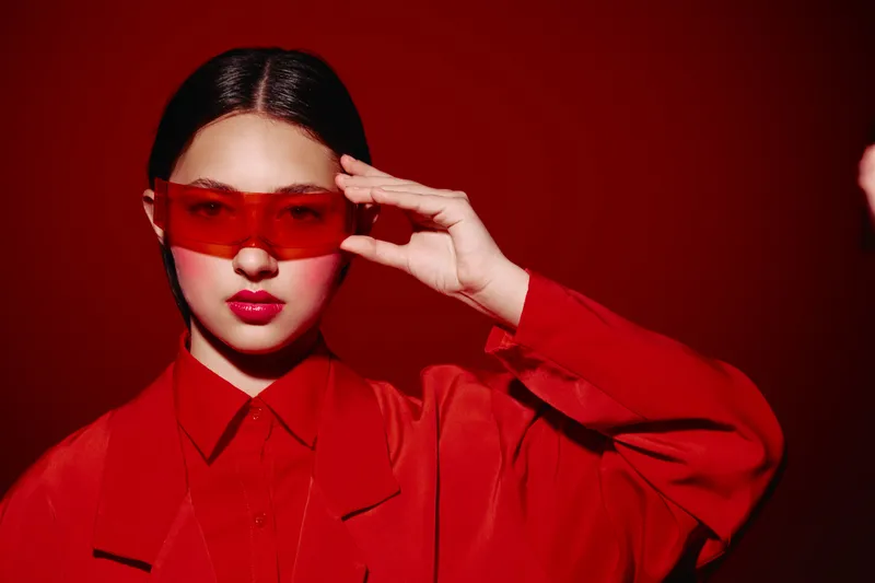 Young woman in red clothing wearing stylish red sunglasses looks confidently at camera. Studio portrait with Matching hues on a bright red background Intense beauty fashion concept.